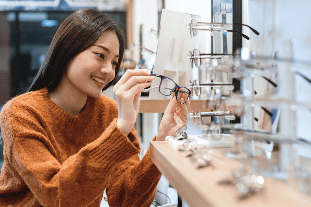 a woman looking at a pair of glasses in an optical